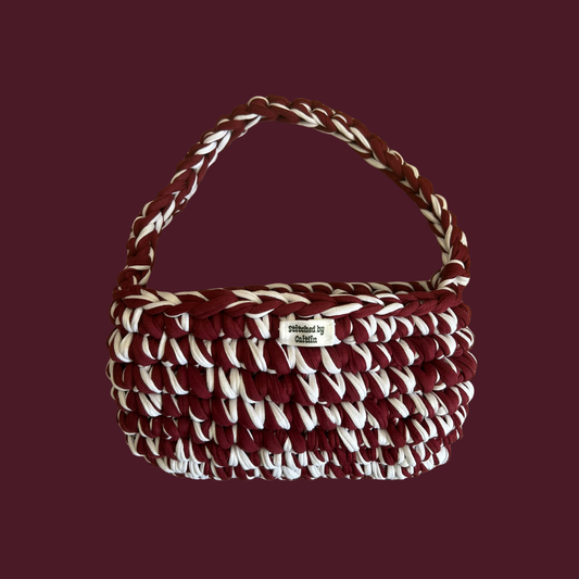 Burgundy and white crocheted bag with a single shoulder strap at the top and a Stitched by Caitlin label on the front