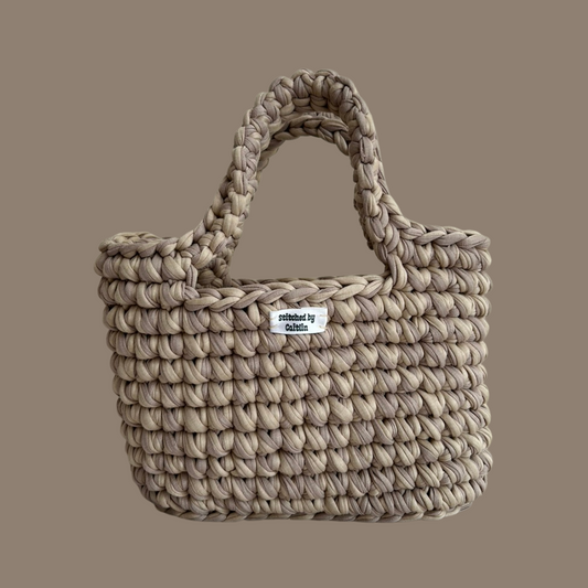 Light and medium brown crocheted bag with two long handles at the top and a Stitched by Caitlin label on the front