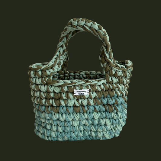 Seaweed green, mint and turquoise crocheted bag with two long handles at the top and a Stitched by Caitlin label on the front