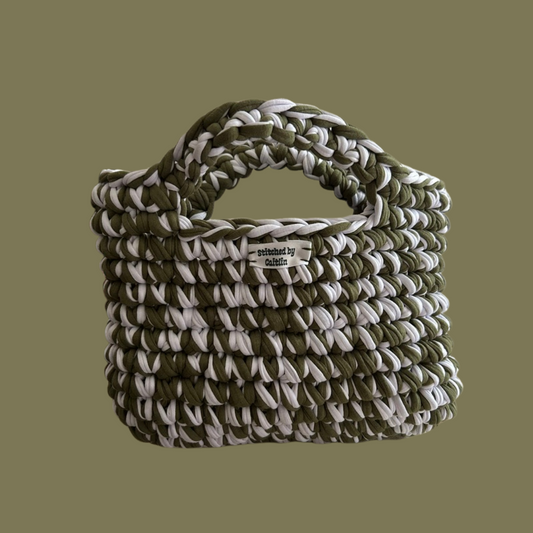 Seaweed green and white crocheted bag with two small handles at the top and a Stitched by Caitlin label on the front