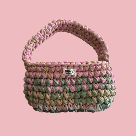 Pink, beige, mint green, white and turquoise crocheted bag with a single shoulder strap at the top and a Stitched by Caitlin label on the front